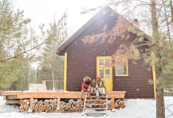 Cabin in a snow filled woods with a family sitting on the front steps
