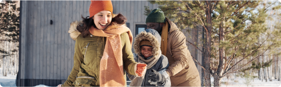 family plays in snow outside cabin