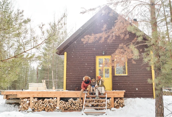Cabin in a snow filled woods with a family sitting on the front steps